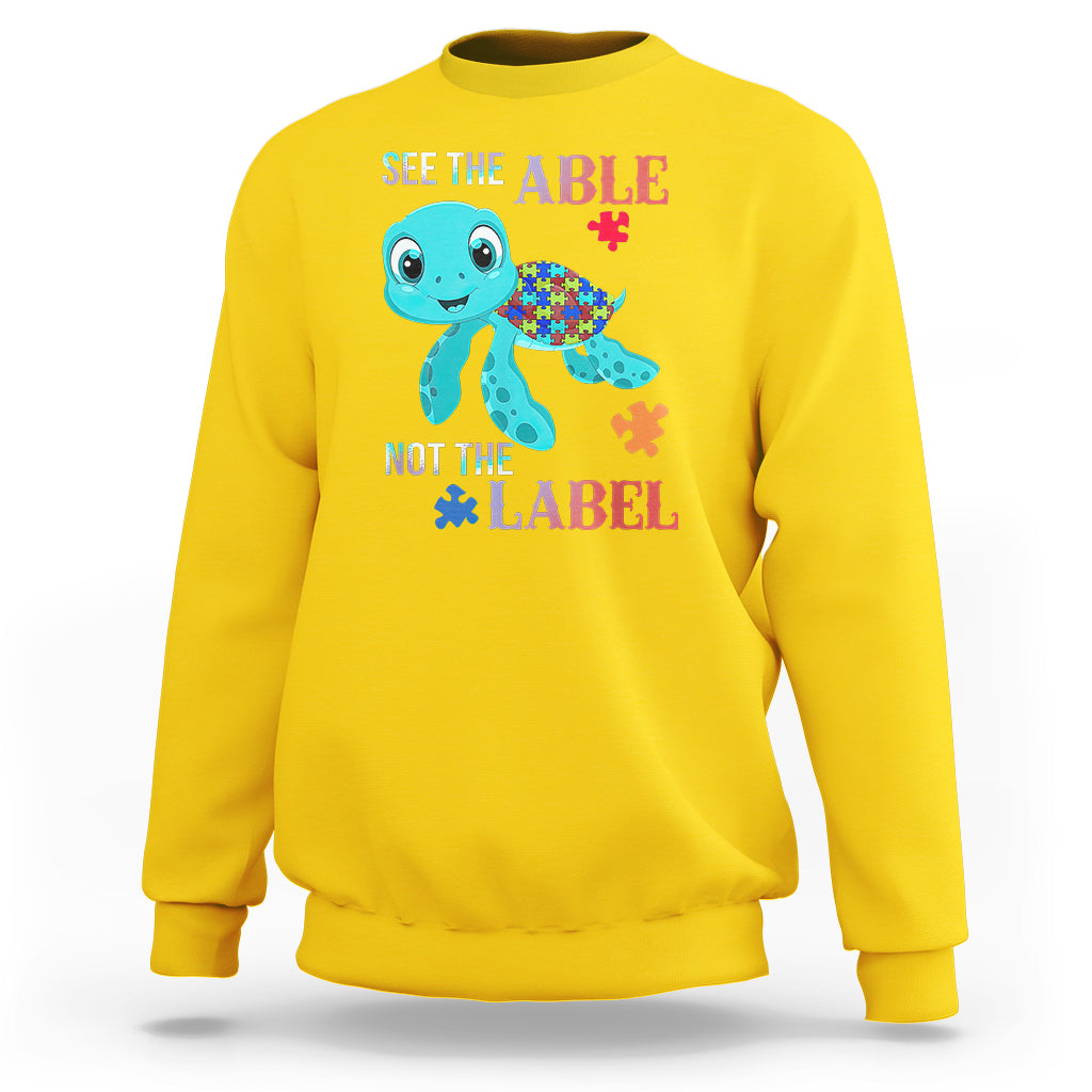 Yellow autism sweatshirt with cartoon turtle and puzzle-piece graphics, “See the Able, Not the Label”