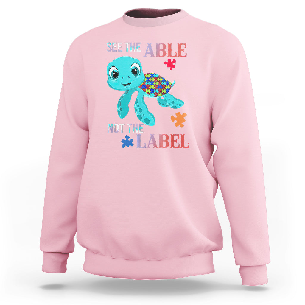 Light pink autism sweatshirt with cartoon turtle and puzzle-piece graphics, “See the Able, Not the Label”