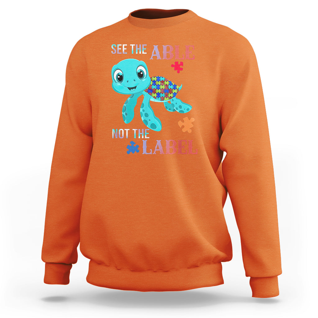 Orange autism sweatshirt with cartoon turtle and puzzle-piece graphics, “See the Able, Not the Label”