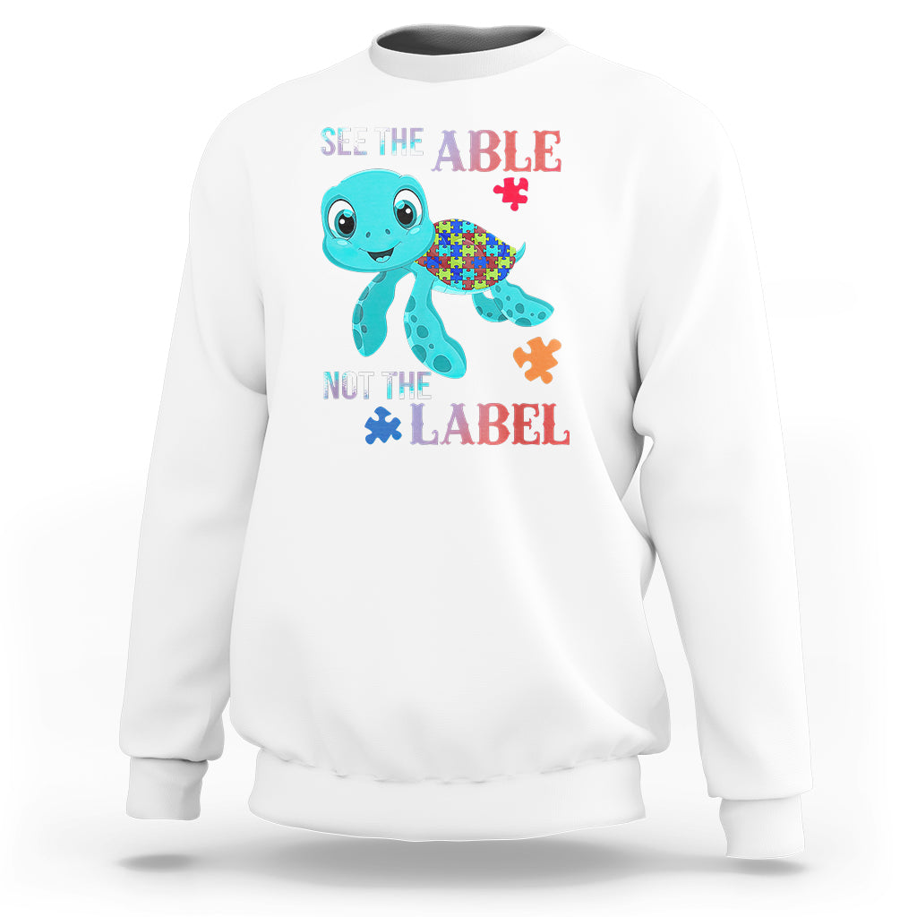 White autism sweatshirt with cartoon turtle and puzzle-piece graphics, “See the Able, Not the Label”