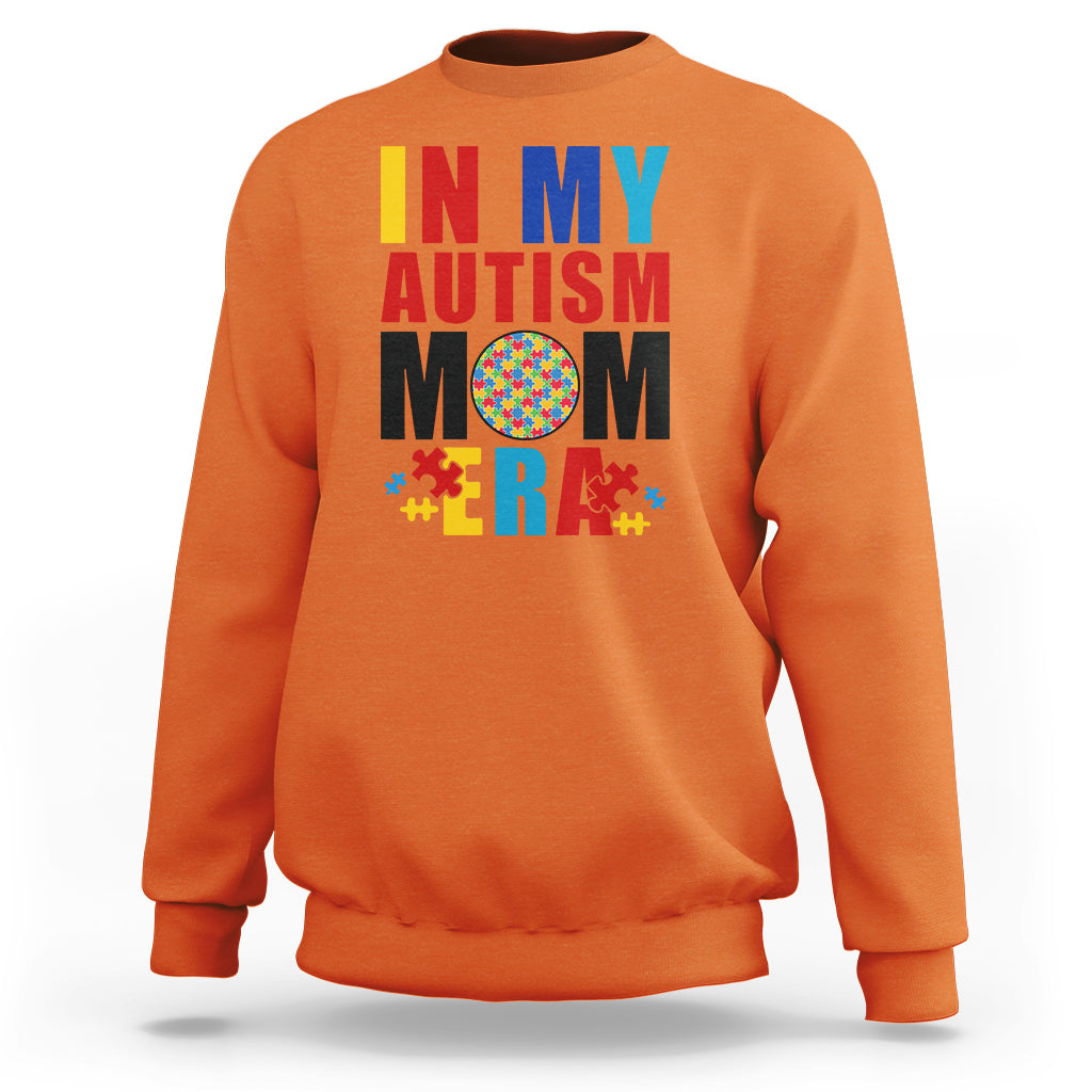 Orange sweatshirt with colorful Autism Mom puzzle-piece graphic, crewneck long sleeves.