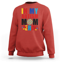 Red sweatshirt with colorful Autism Mom puzzle-piece graphic, crewneck long sleeves.
