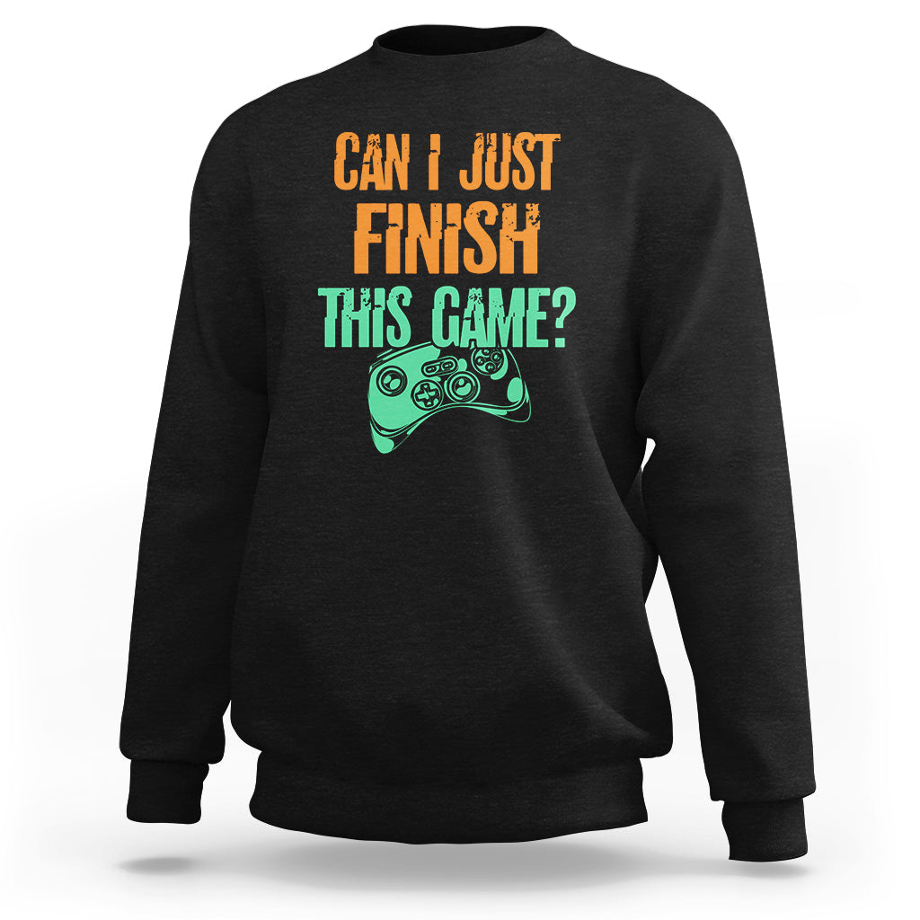 Black crewneck sweatshirt with colorful “Can I just finish this game?” gamepad graphic.