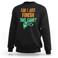 Black crewneck sweatshirt with colorful “Can I just finish this game?” gamepad graphic.
