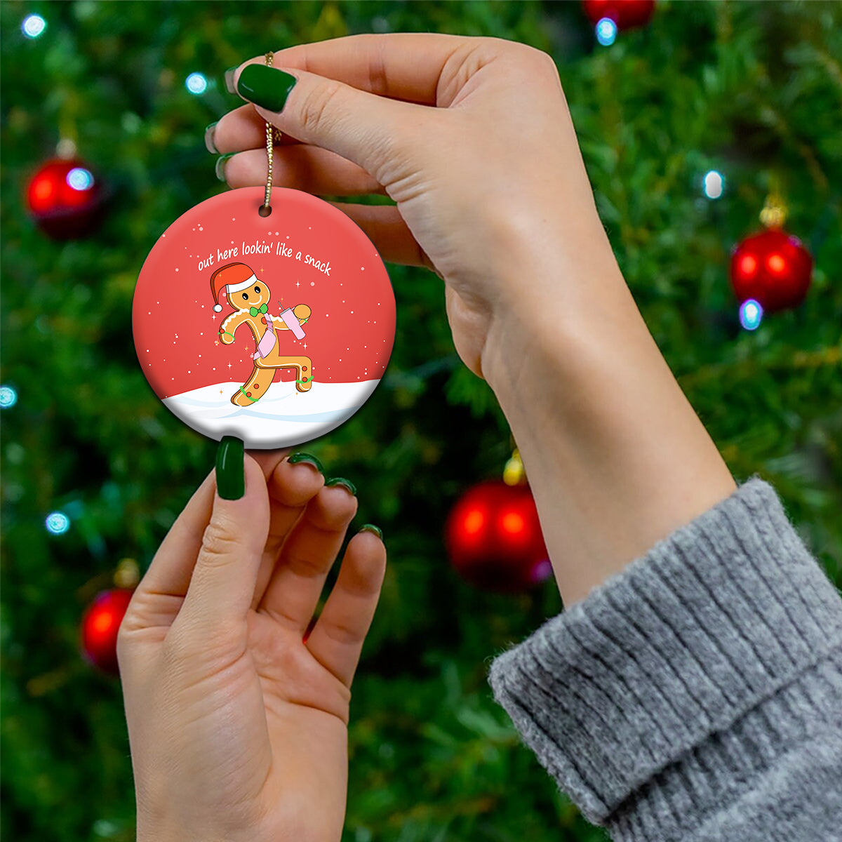 Red round ceramic ornament held by hands, featuring gingerbread runner and gold loop.