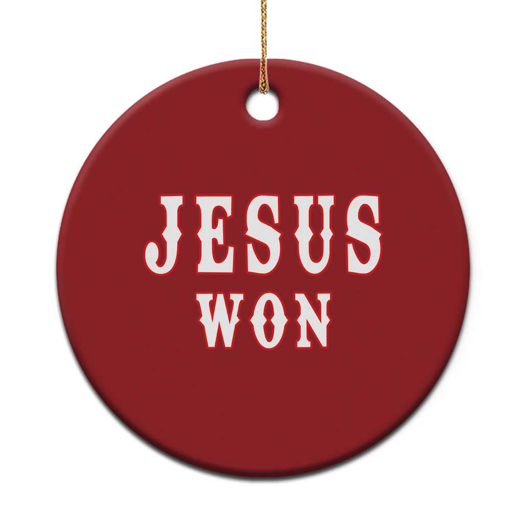 Red round Christmas ornament with 'JESUS WON' lettering, hanging with gold string.