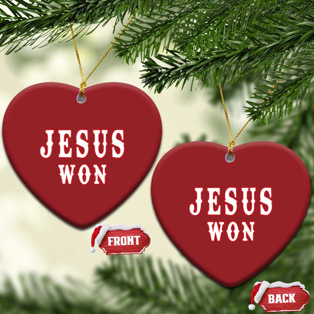 Red heart-shaped ornament with 'JESUS WON' text, hung on gold cords.