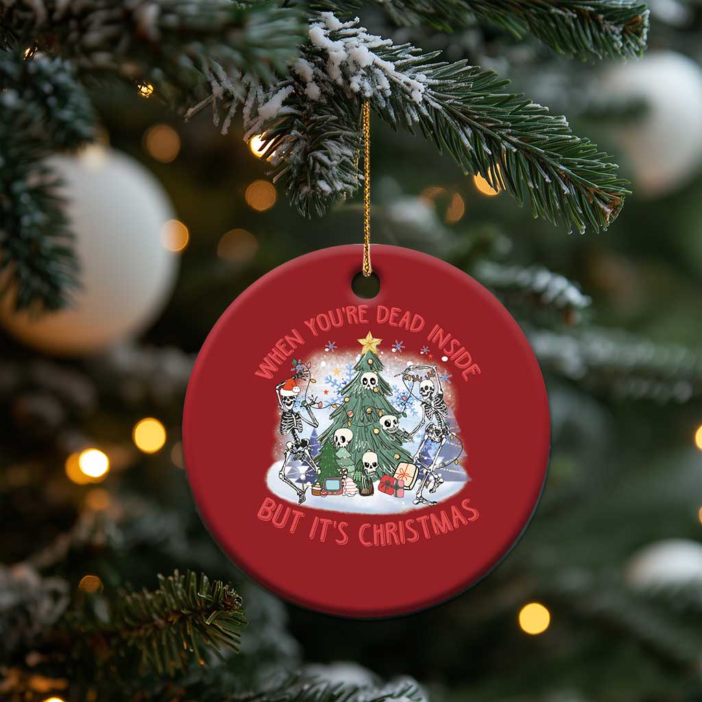 Red round Christmas ornament hanging on a tree branch, with skeletons around a tree