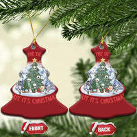 Two red bell-shaped Christmas ornaments hanging on evergreen branches