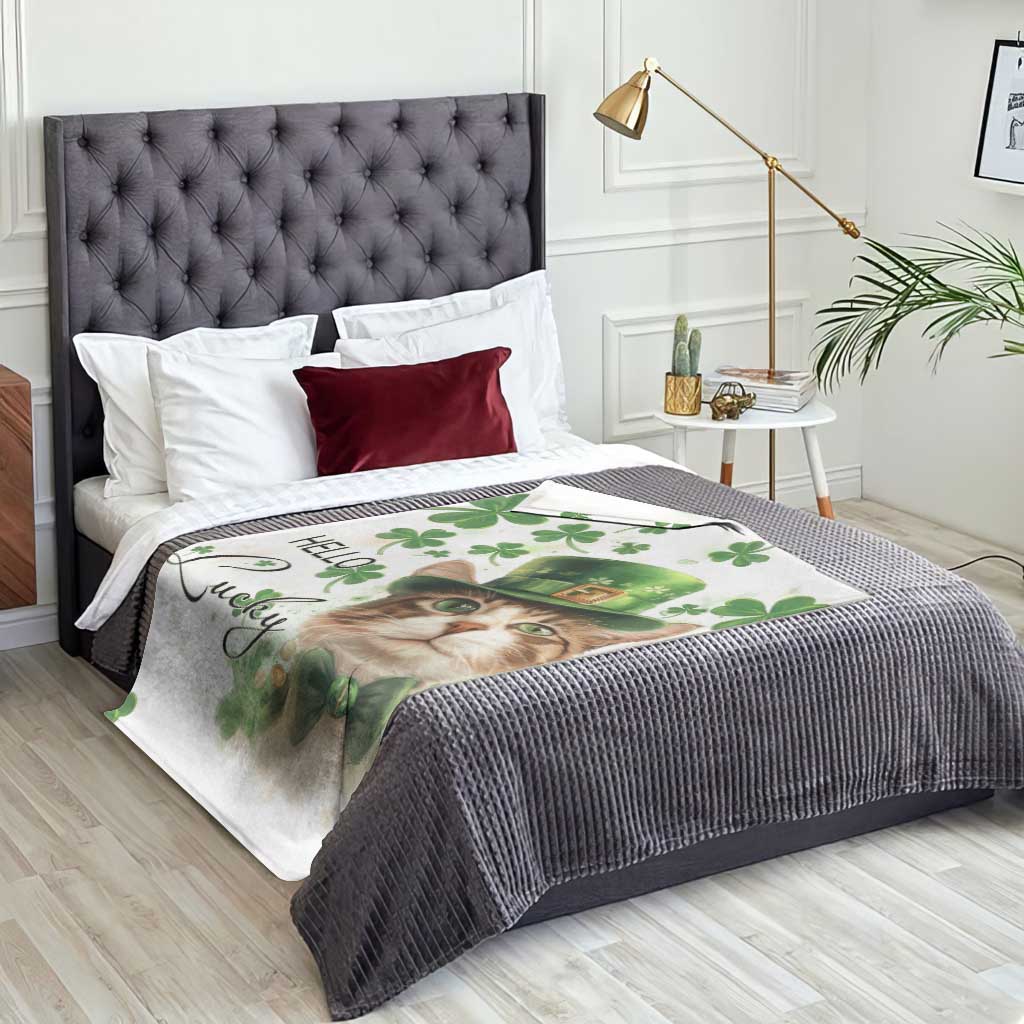 Cat-themed throw blanket on a bed: white fabric with green clovers, leprechaun hat, “Hello Lucky”