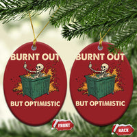 Two red oval Christmas ornaments with skeleton dumpster art and “Burnt out, but optimistic”.