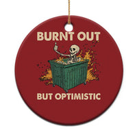 Red round Christmas ornament with skeleton in a dumpster and text “Burnt out, but optimistic”.