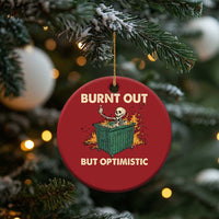 Red round Christmas ornament with skeleton-in-dumpster graphic and “Burnt out, but optimistic”.