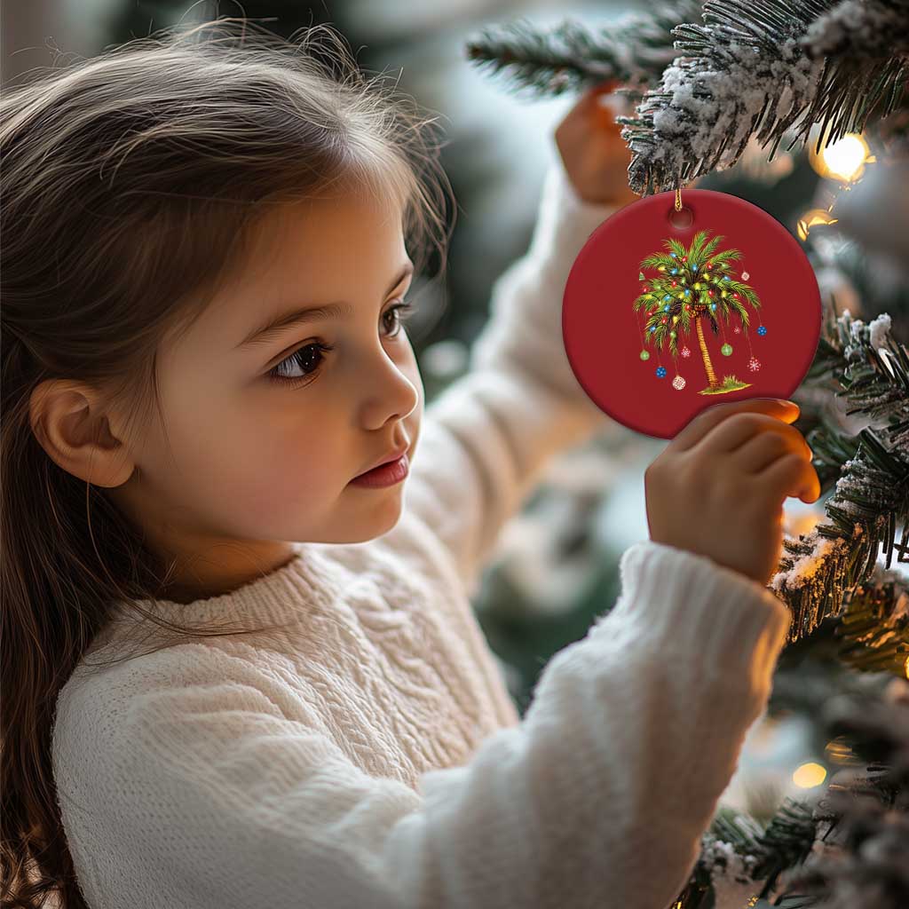 Red round palm tree ornament with multicolor lights held by a child, gold hanging loop.