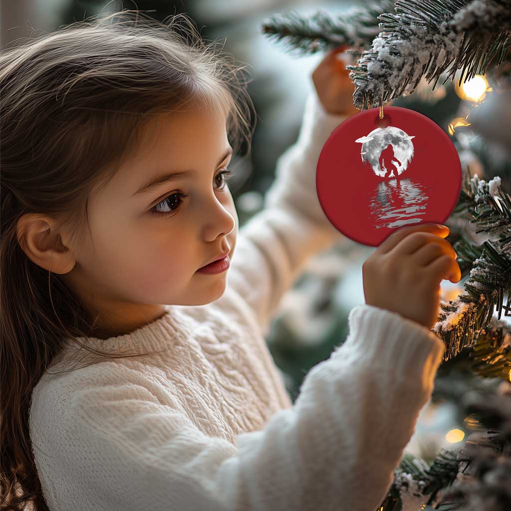 Red circular Bigfoot Christmas ornament being held, silver moon design, gold string