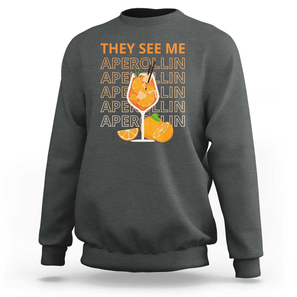 Dark heather sweatshirt with “THEY SEE ME” Aperol-lin text and citrus cocktail graphic on back