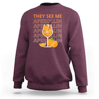 Maroon sweatshirt with “THEY SEE ME” Aperol-lin text and citrus cocktail graphic on back