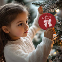 Child holding red round Christmas ornament with pink bow and gold hanging string