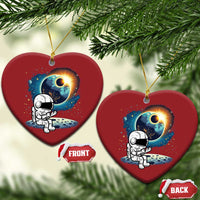 Two red heart-shaped astronaut space ornaments hanging from pine branches