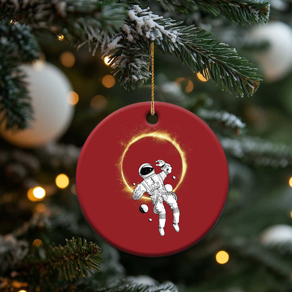 Red circular astronaut ornament with glowing halo ring, hanging from a gold string