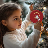 Red circular astronaut ornament with glowing halo ring, hanging on a pine tree