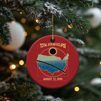 Red circular solar eclipse map ornament hanging from a pine tree branch