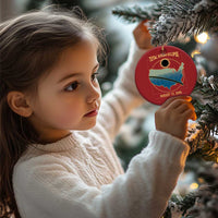 Child holds a red circular solar eclipse map Christmas ornament from the tree