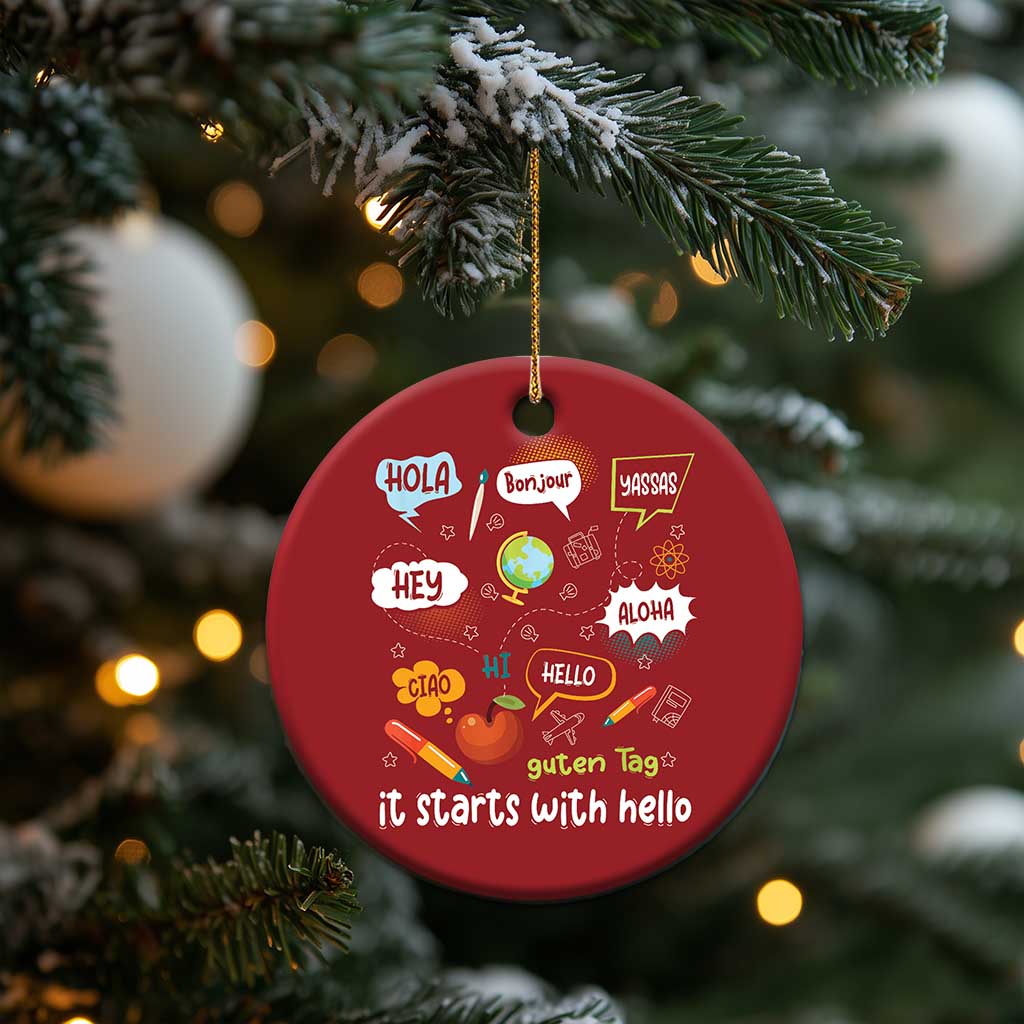 Red round Christmas ornament with “it starts with hello” and language greetings, on gold string.
