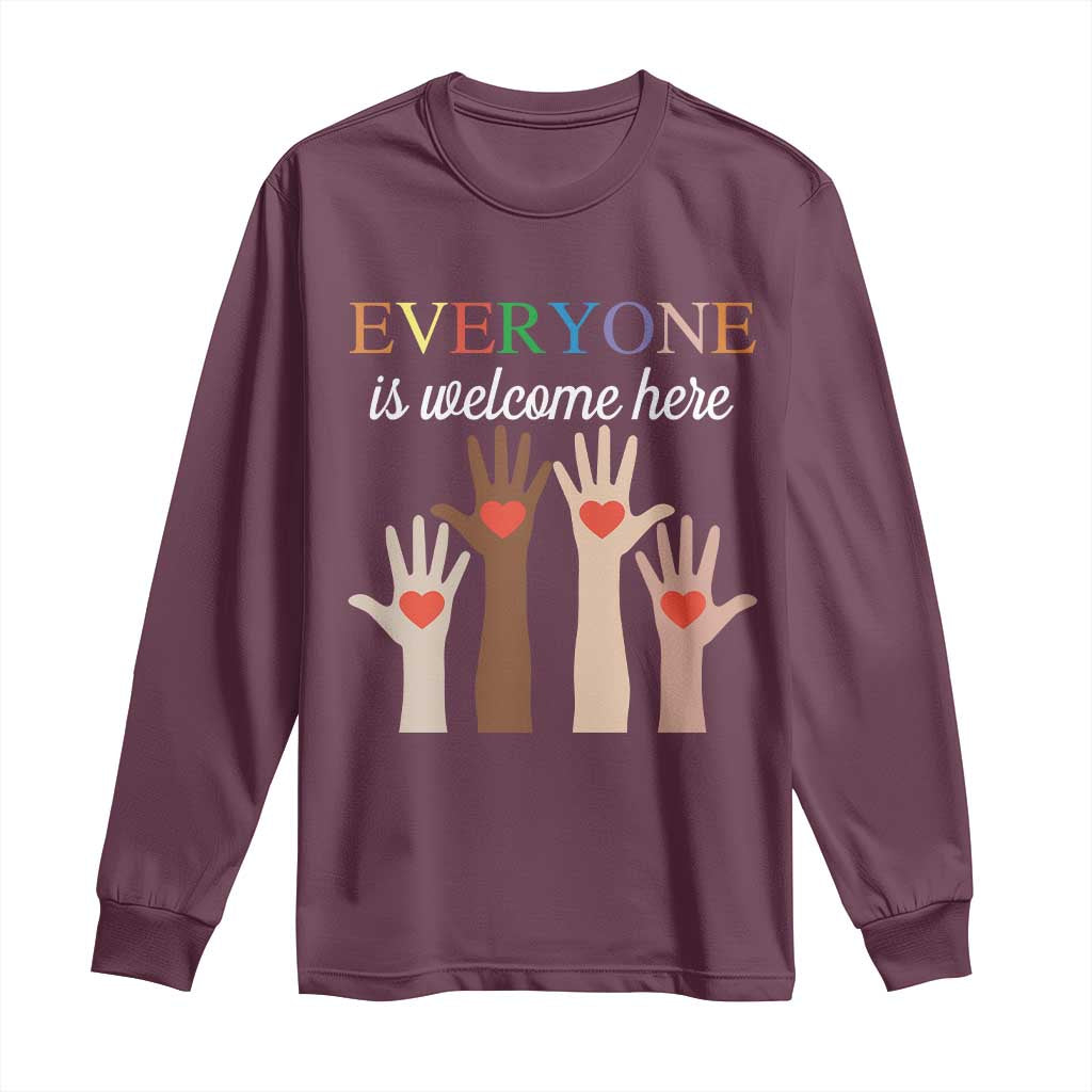 Maroon long sleeve shirt with “Everyone is welcome here” heart-hand graphic