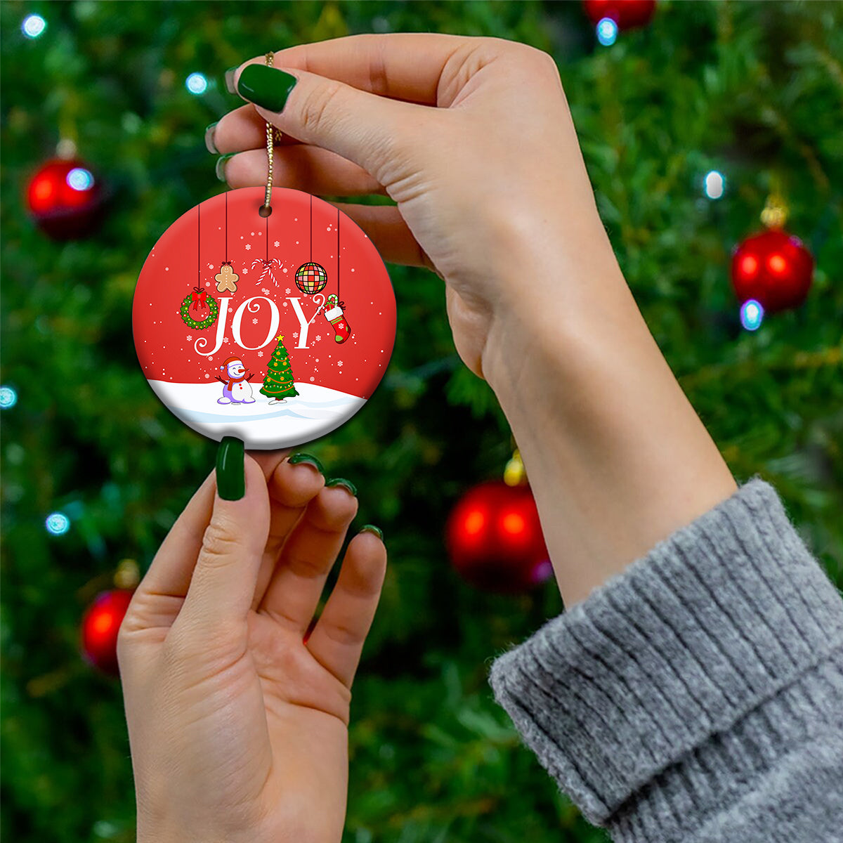 Round red “JOY” ceramic ornament held by hands with gold hanging loop.