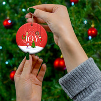 Round red “JOY” ceramic ornament held by hands with gold hanging loop.