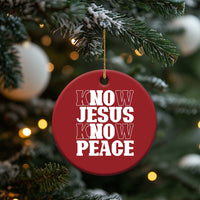 Red circular Christmas ornament hanging from a gold string, “KNOW JESUS KNOW PEACE” in white.