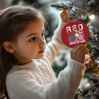 Red round Christmas ornament on tree branch with "Support Our Troops" text and gold hanger