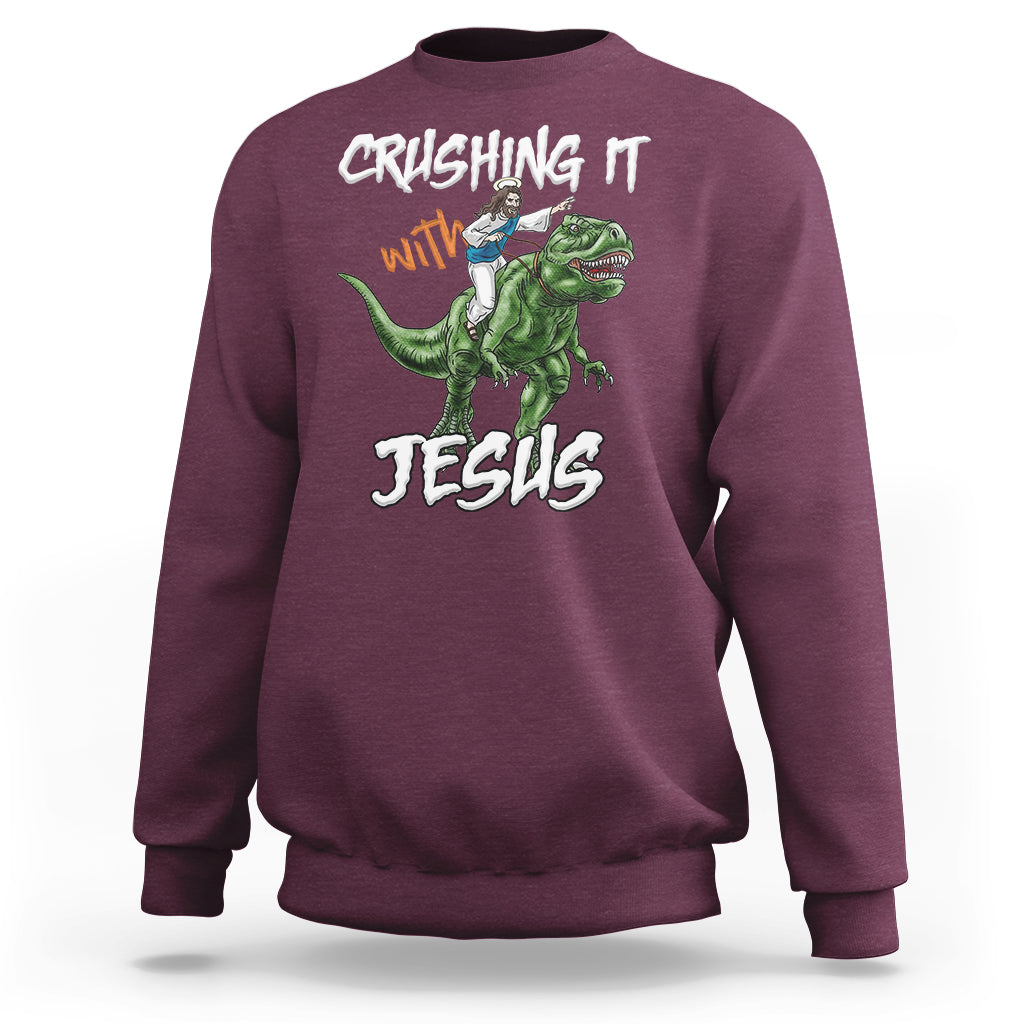 Maroon crewneck sweatshirt with dinosaur graphic and text "CRUSHING IT with JESUS"