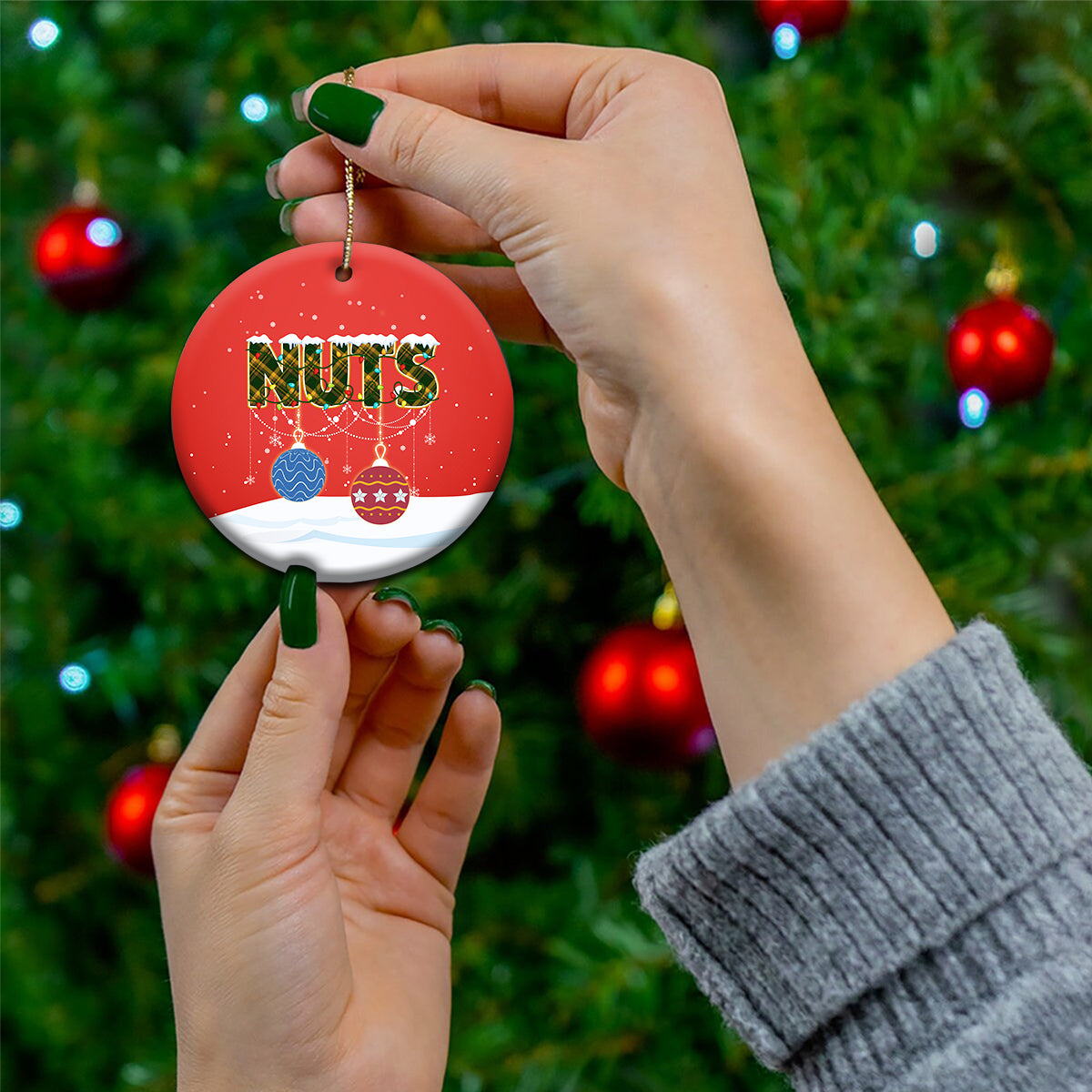 Red ceramic round Christmas ornament labeled “NUTS,” held by a hand with gold string.