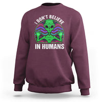 Maroon crewneck sweatshirt with green alien graphic and “I don’t believe in humans” text