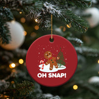 Red circular “OH SNAP!” gingerbread ornament hanging from a gold string on a Christmas tree