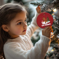 Red circular “OH SNAP!” gingerbread ornament being held near evergreen branches