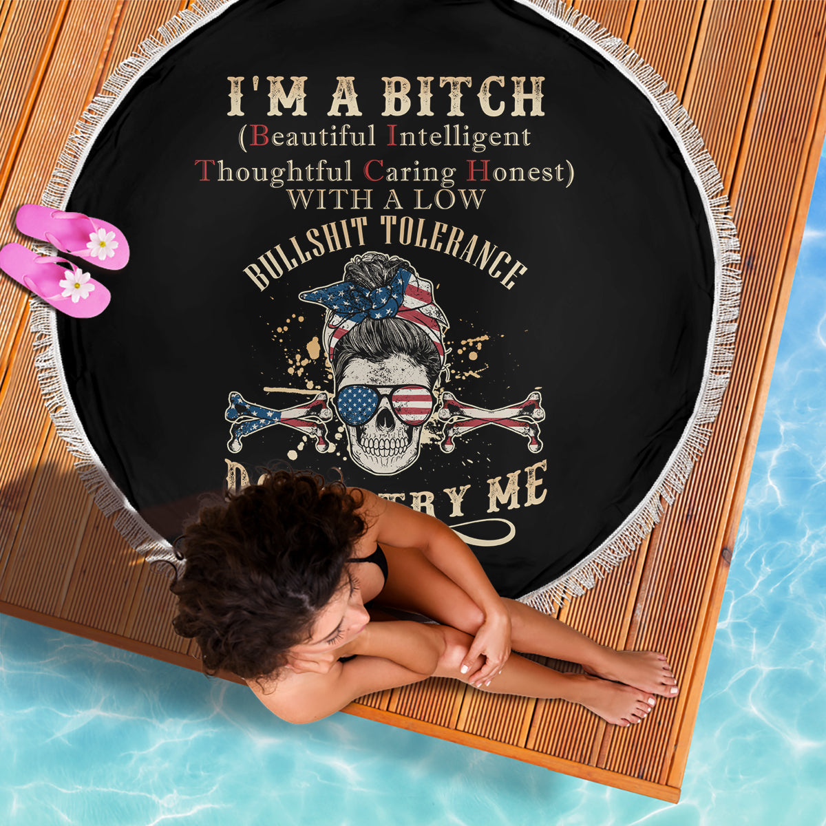 Round black beach blanket with fringed edge and skull pirate graphic, text center.
