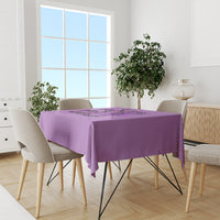 Purple tablecloth on dining table with chairs and potted plant on side.