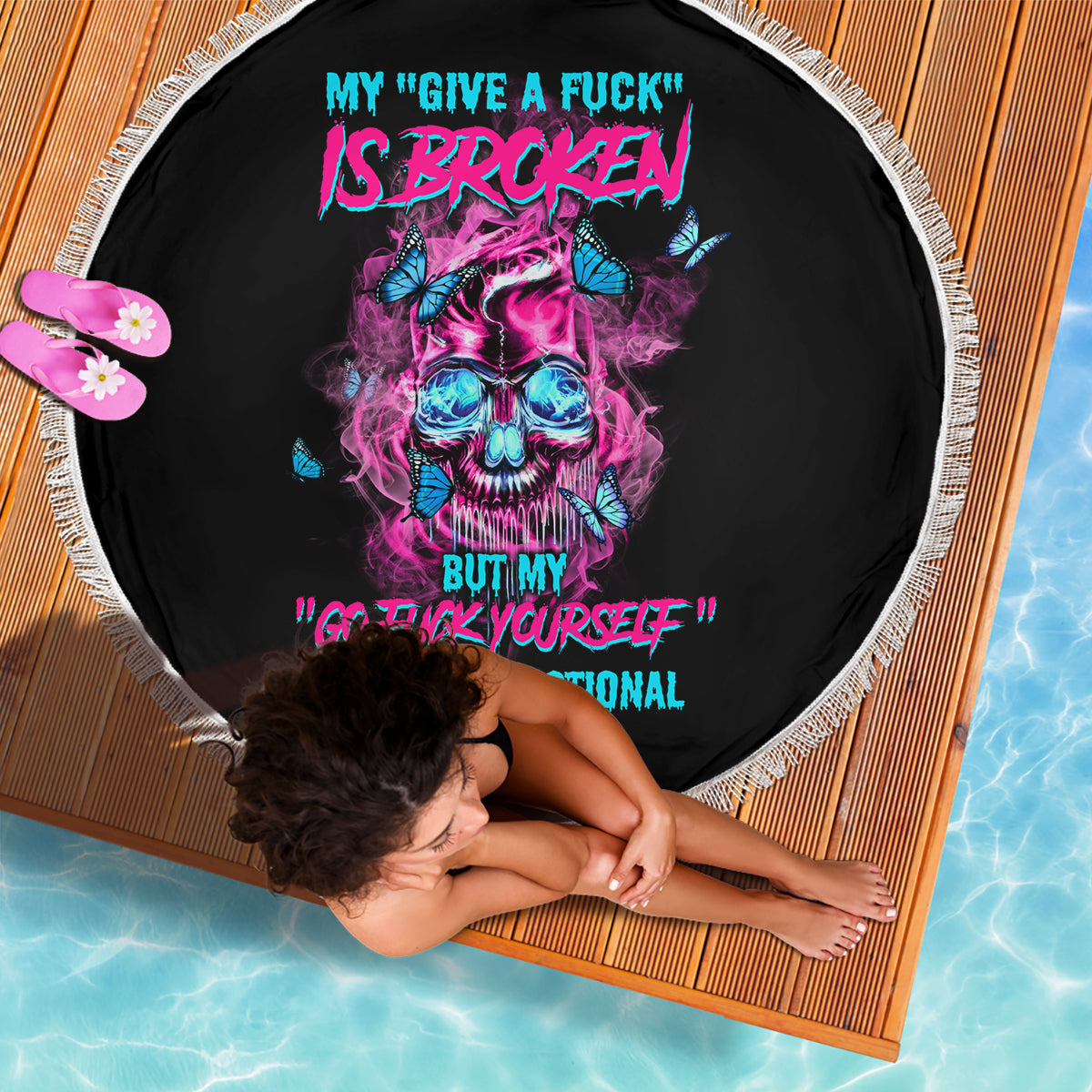 Round black beach blanket with fringed edge, neon skull and quote graphic.