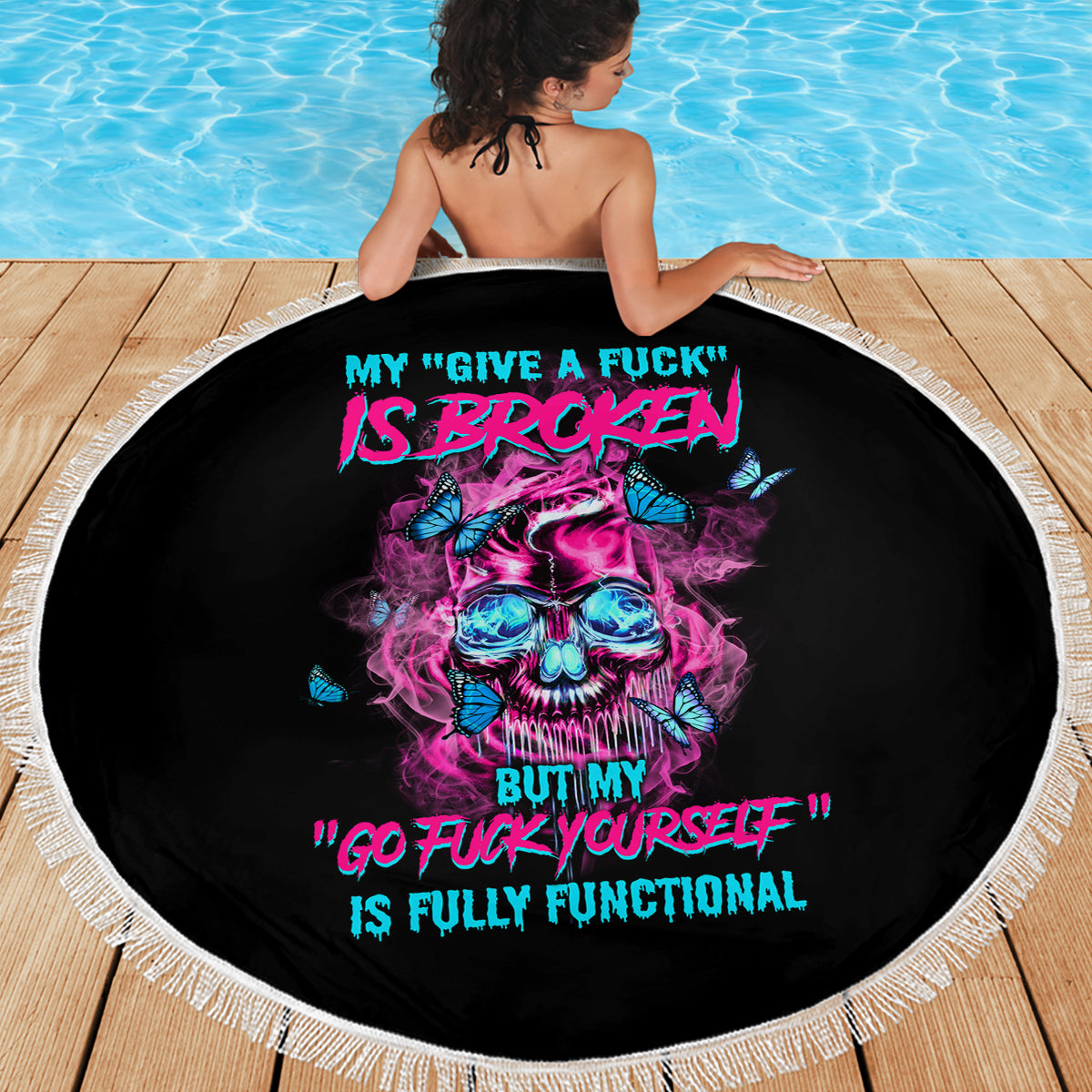 Round black beach blanket with fringed edge, neon skull and quote text shown in use.
