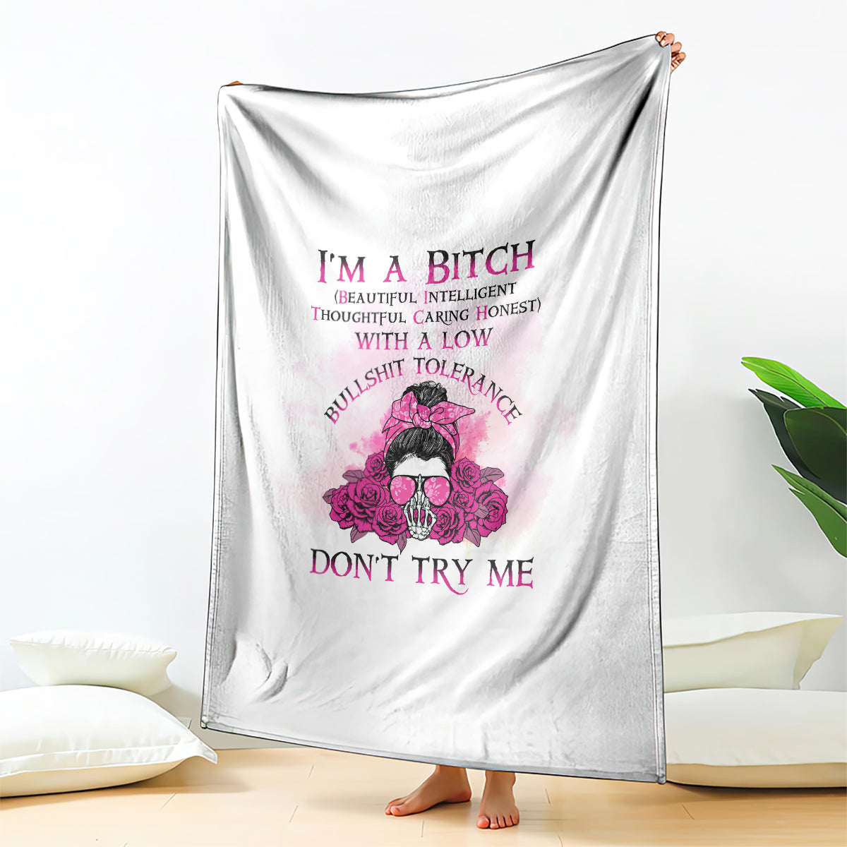 White blanket hanging with pink floral skull graphic and stacked purple text, full view.