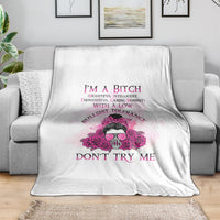 White fleece blanket with pink floral skull graphic and bold purple text, draped on sofa.