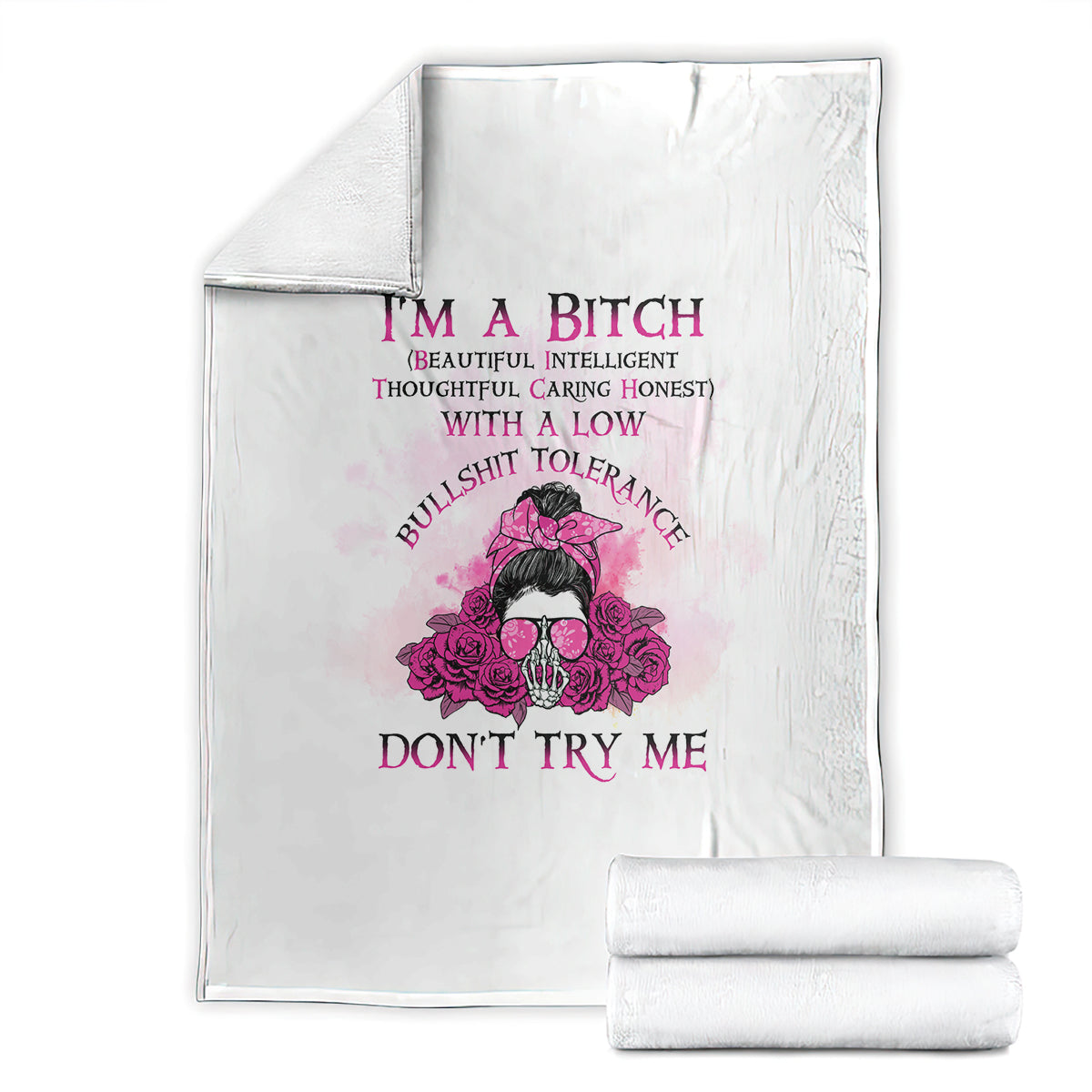 White blanket laid flat with pink floral skull graphic and purple text, with rolled blanket.