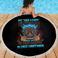 Black round beach blanket with white fringed edge showing colorful tiki skull graphic