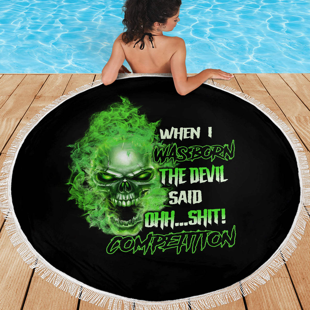 Round beach blanket laid out on wood, black with neon-green skull graphic and white fringe