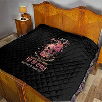Black quilt blanket on a bed with diamond pattern and central pink flower skull graphic