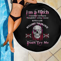 Black round beach blanket with fringe border and skull with crossed bones graphic in pink