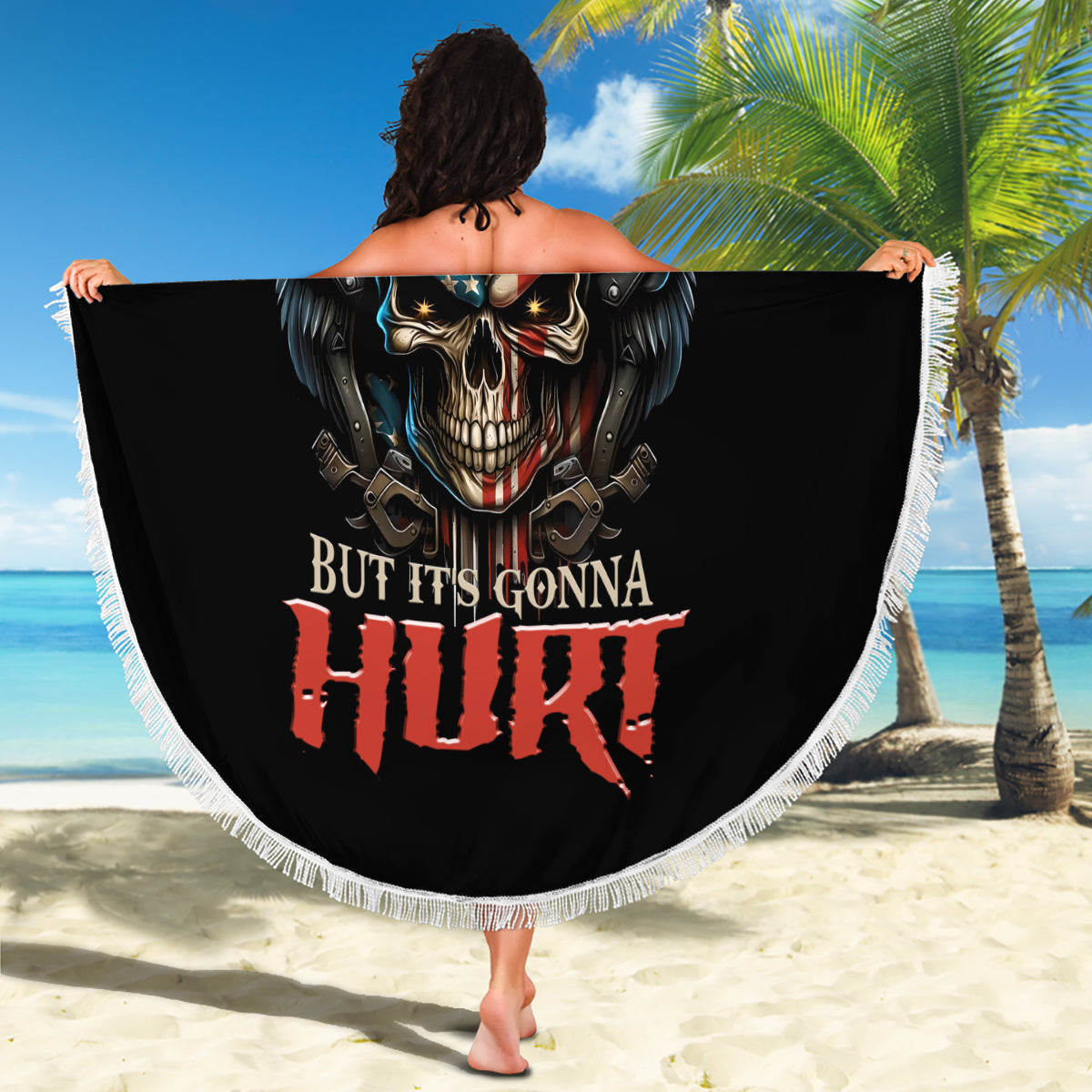 Round black beach blanket held up outdoors, skull graphic with wings and text, fringe